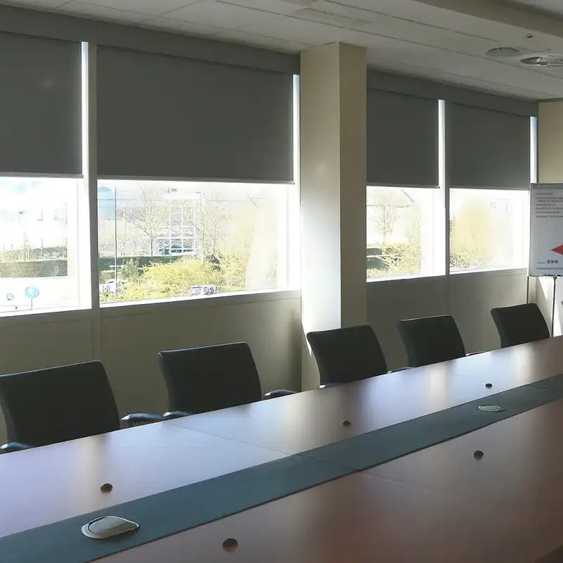 Modern grey roller blinds in a bright corporate boardroom.